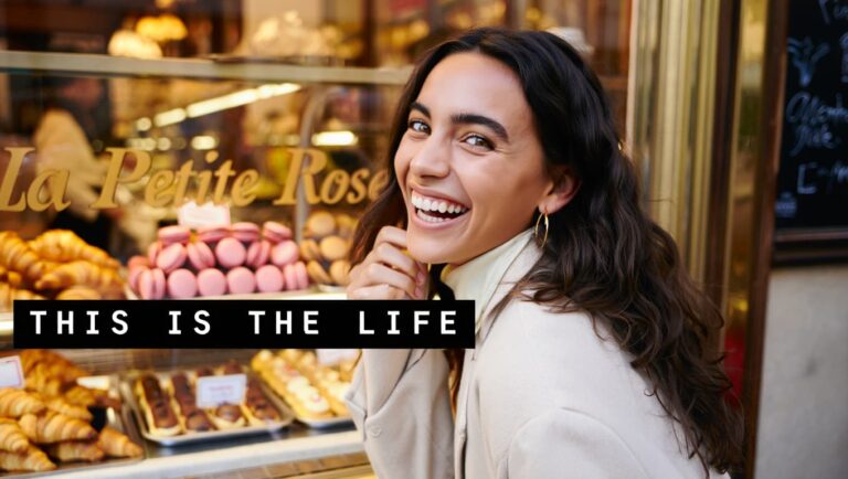 A beautiful confident woman laughing genuinely, warm golden light, soft bokeh background, outdoor or cozy café setting, warm rose and amber tones, bold black text box overlay in lower third reading